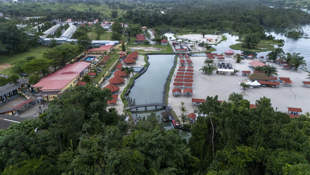 Aerial view of McCarthy beach featuring sandy shores, rows of red-roofed cabanas, swimming pools, and a wooden bridge crossing a river in Urhuoka, Delta, Nigeria.