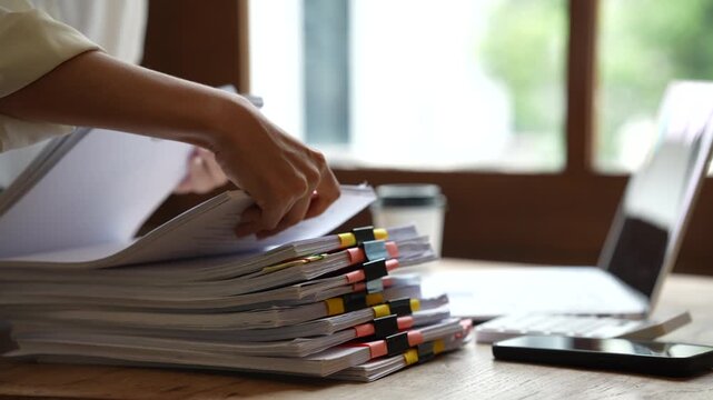 Business professional working on a laptop while managing stacks of organized documents and paperwork in a bright modern office.