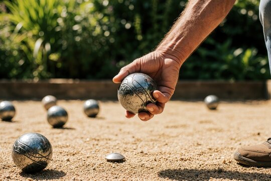 Man grips metal petanque ball ready to throw. He concentrates on aiming for target on gravel court. Other balls lie on ground near him.