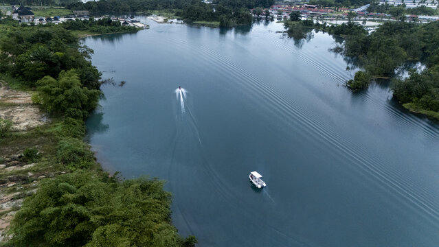 Aerial view of a boat and a jet ski cruising on the calm blue waters of a lake surrounded by lush green vegetation and trees in Urhuoka, Delta, Nigeria.
