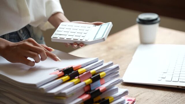 Business professional working on a laptop while managing stacks of organized documents and paperwork in a bright modern office.