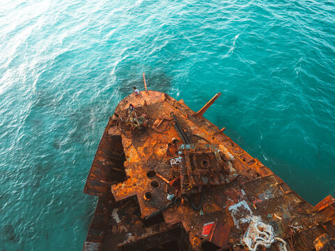 Aerial view of the rusted Gulf Dove shipwreck resting in turquoise waters with people standing on the deck in Hulaf, Yemen.