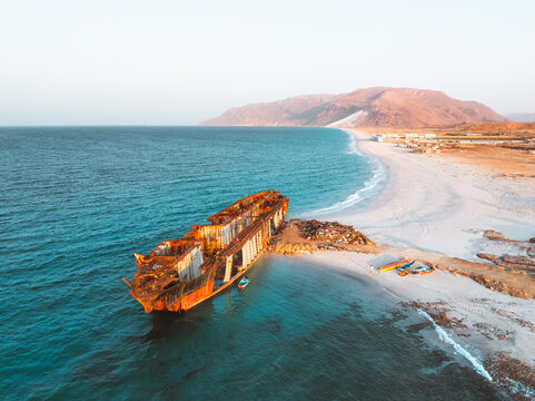Aerial view of Gulf Dove shipwreck resting on the sandy beach with turquoise waters and arid coastal mountains in the background Hulaf, Yemen.