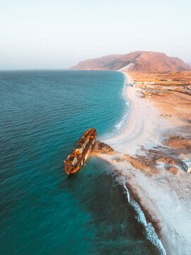 Aerial view of the rusted Gulf Dove shipwreck resting on the white sandy beach near the turquoise waters of the Arabian Sea, Hulaf, Yemen.