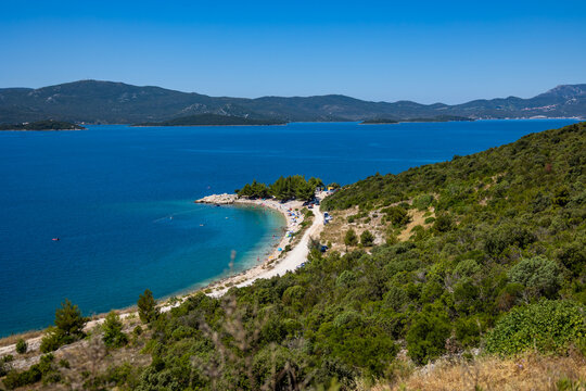 An aerial view of a secluded beach along a blue sea surrounded by green hills under a clear sky in Croatia.