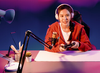 Host channel of beautiful Asian girl streamer with joystick playing online game wearing headphones pastel color talking with viewers media online. Esport skilled team players in neon room. Stratagem. © InfiniteFlow