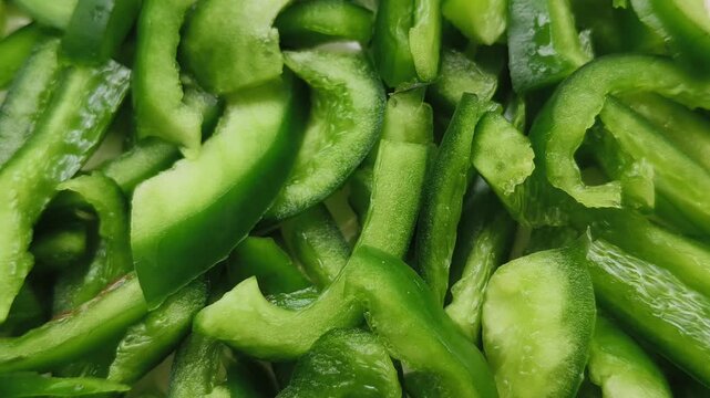 Chopped green color capsicum, bell pepper or paprika vegetable fruit long cut piece slices pile or heap background. Closeup slow spinning or rotating top view. Healthy vegan diet cooking concept.