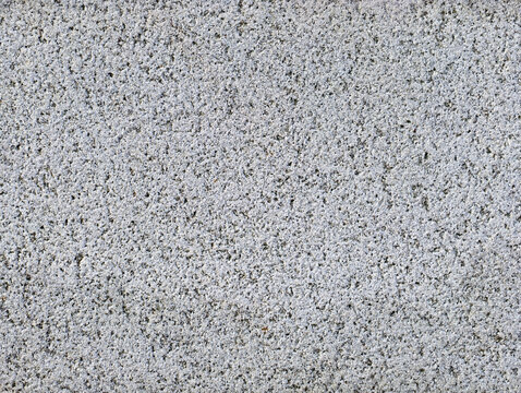 A close view of a granite surface reveals its texture and small flecks. The light shines at an angle, highlighting the differences in shades. The setting is indoors