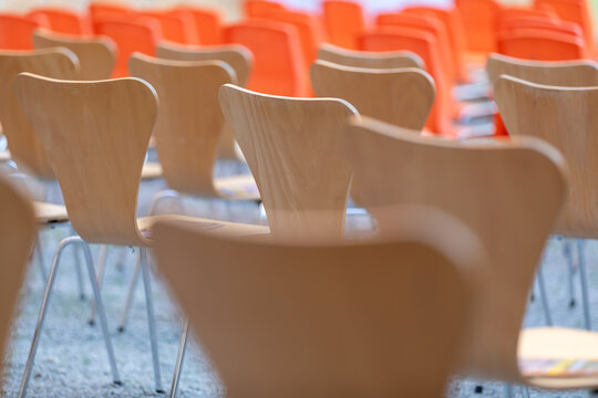 The backs of empty wooden chairs arranged in rows for a public event.	
