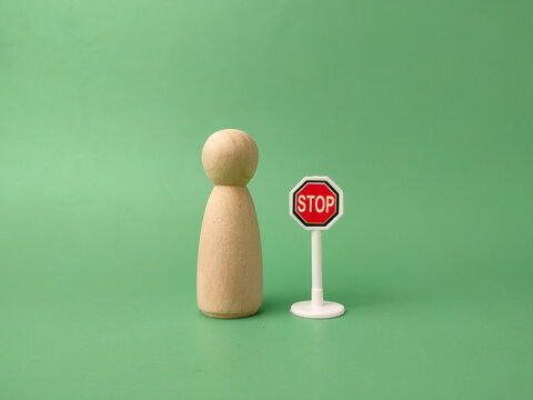 A single wooden peg figure stands next to a miniature red stop sign on a plain green background