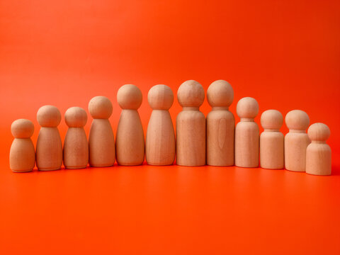 Eleven wooden peg figures of varying heights stand arranged in a symmetric wave line on an orange background
