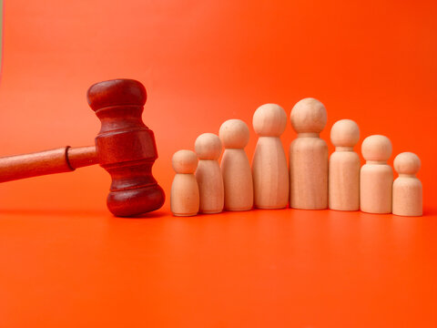 A wooden gavel rests beside eight wooden peg figures arranged by height on a vivid orange background