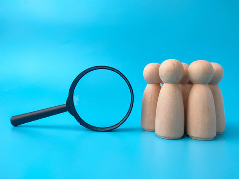 A black magnifying glass lies beside a cluster of wooden peg figures arranged on a vibrant blue background