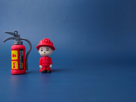 A toy fire extinguisher stands beside a winking firefighter figurine on a solid blue background
