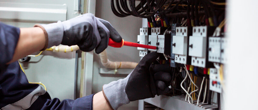 Maintenance service of industrial power distribution board by skilled technician with safety gloves.