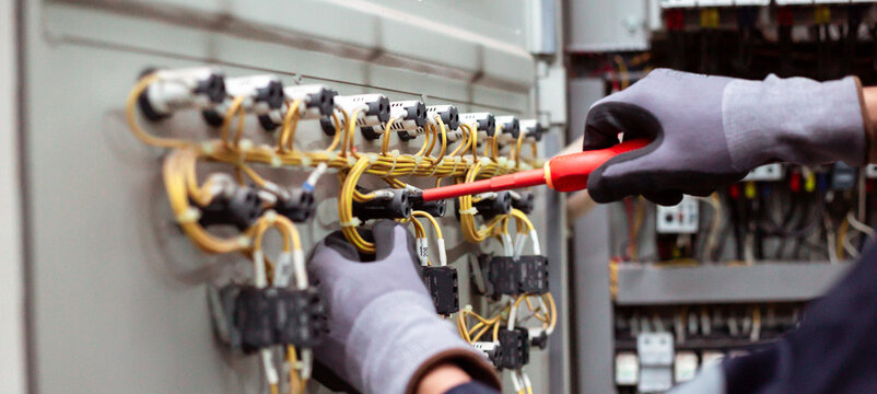 Close-up of electrician hands wiring and connecting components on electrical control panel door.