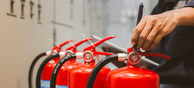 Technical engineer inspecting a row of red fire extinguishers during routine safety service in an industrial building corridor.