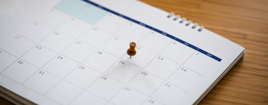 Close up of calendar page with thumbtacks on important dates.