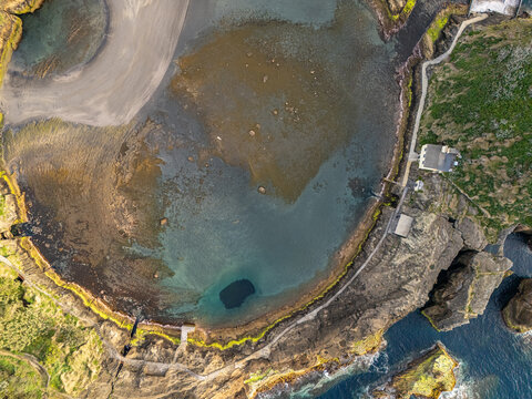 Aerial view of Ilheu de Vila Franca do Campo, a volcanic islet with a circular crater lake, rocky coastline, and lush green vegetation in Sao Pedro, Acores, Portugal.