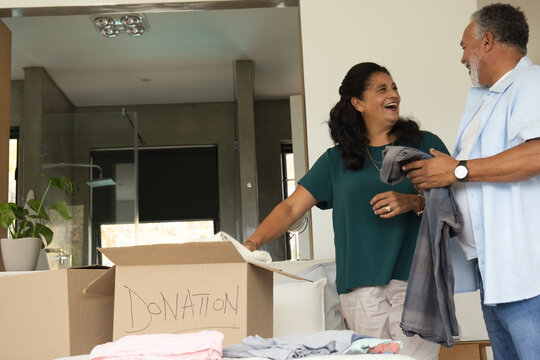 Mature African couple smiling while sorting clothes into box labeled DONATION at home, copy space