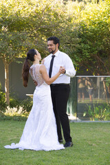 Couple dancing on lawn, bride in white lace gown train, groom black tie, glass railing reflecting © wavebreak3