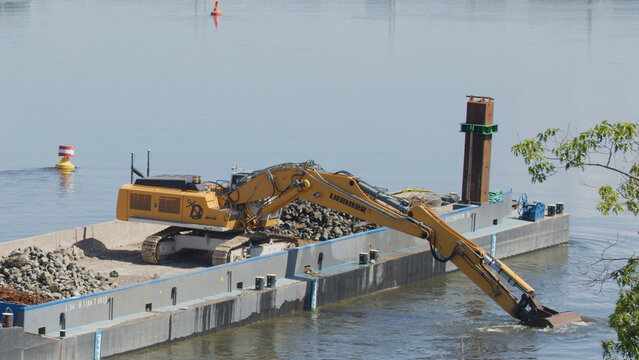 Yellow Hydraulic Excavator Unloading Rocks from a Barge on the Elbe River