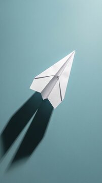 White paper airplane in direct light casting a dramatic shadow on a blue background