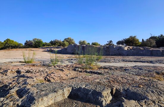 Photo of the ancient Pnyx archaeological site in Athens, Greece, featuring weathered limestone bedrock, historic assembly terrace walls, and a clear summer afternoon sky. 