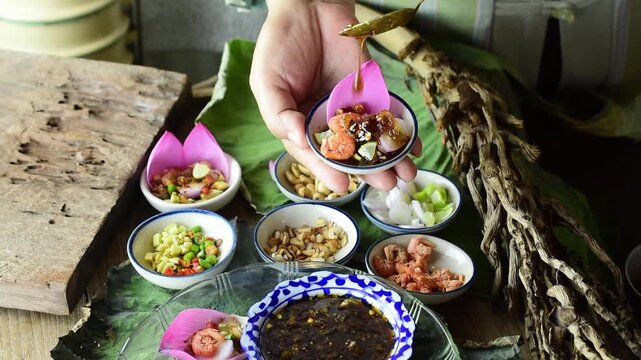 Chef pouring sweet sauce on traditional Thai lotus petal Miang Kham snack with fresh ingredients, herbs and spices served in small porcelain bowls for healthy authentic Asian food culture footage.