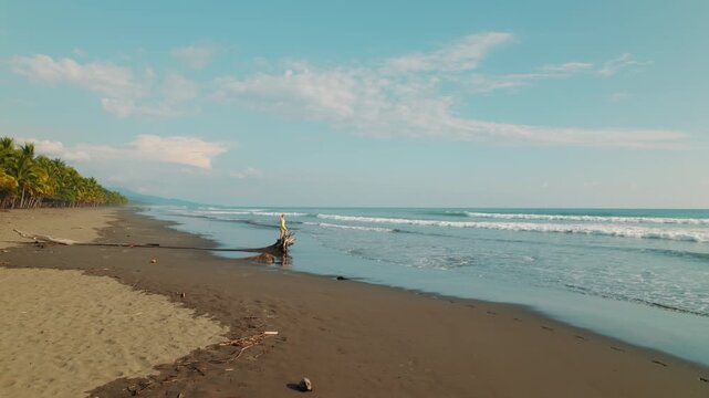 Person standing on driftwood along empty beach at sunset in Costa Rica