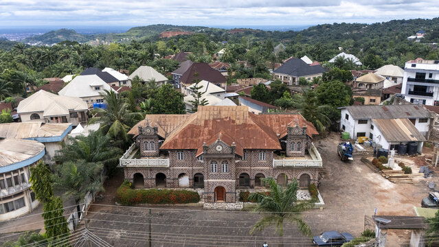 Aerial view of the historic stone building with a rusted metal roof surrounded by lush tropical trees and residential houses in Ngwo, Enugu, Nigeria.