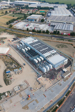 Aerial view of the BYES MIL08 data center facility featuring rooftop solar panels and industrial cooling units, surrounded by construction areas and warehouses, Siziano, Lombardia, Italy.