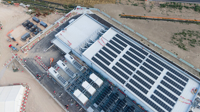 Aerial view of BYES MIL08 data center with rooftop solar panels, industrial cooling units, and surrounding construction site in Siziano, Lombardia, Italy.