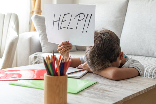 Young boy struggling with schoolwork, hiding his face on a desk and holding up a sign with help!! written on it, depicting educational challenges and learning difficulty