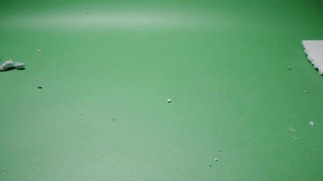 White gypsum board shattering with dynamic impact on a green studio background during a controlled demolition