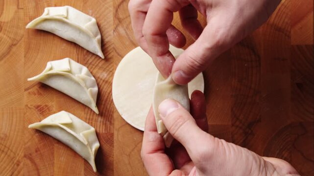 Timelapse shows hands sealing gyoza by pressing wrapper edges. Tutorial shows gyoza folding technique for tight seal and no leaks. Teach gyoza in cooking class, recipe video, blog or online guide.