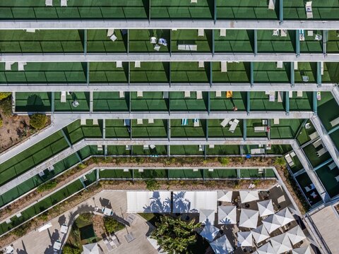 Aerial view of a modern hotel building with rows of balconies featuring green artificial turf and lounge chairs, overlooking a patio area with white umbrellas in Cascais, Lisboa, Portugal.