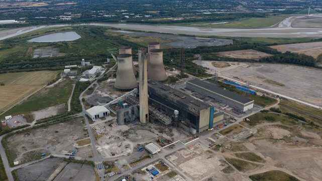 Aerial view of the decommissioned Fiddlers Ferry Power Station with cooling towers and tall chimney surrounded by industrial grounds and fields in Warrington, England, United Kingdom.