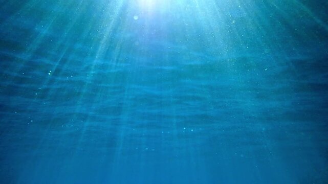 A slow-motion shot of an underwater sea background, sunlight penetrating and reflecting of sea surface. deep undersea. light rays shining through. Dark blue ocean surface seen from under water.
