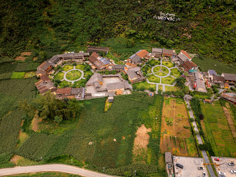 Aerial view of the traditional village in Meo Vac with circular courtyards and rustic houses surrounded by lush green fields and mountainous terrain in Meo Vac, Ha Giang, Vietnam.