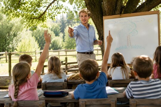 A teacher stands beside a large whiteboard while explaining a lesson to elementary school children outdoors, creating an engaging educational scene centered on curiosity, communication, and active cla