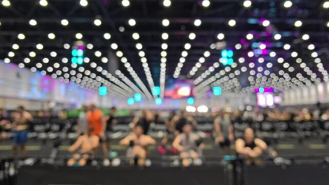 Blur background of Hyrox race row pull competition, Sports arena indoor stadium rowing machine athlete group exercise competition scene with bright ceiling light