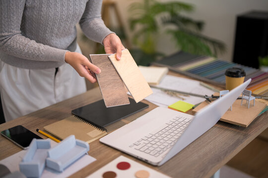 Furniture designer comparing wood and beige material samples on studio workspace with color swatches