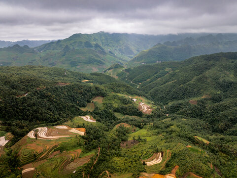 Aerial view of Ha Giang Loop featuring lush green mountains and terraced rice fields under a cloudy sky in Dong Van, Tuyen Quang, Vietnam.