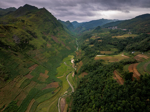 Aerial view of Ha Giang Loop featuring lush green terraced rice fields, a winding river in the valley, and dramatic mountain slopes in Dong Van, Tuyen Quang, Vietnam.