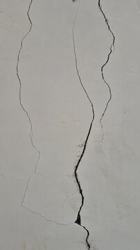 Close-up shot of deep crack on white concrete wall, structural damage concept