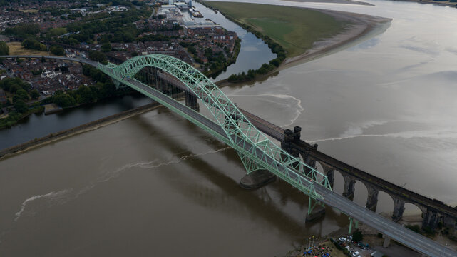 Aerial view of the Silver Jubilee Bridge spanning the River Mersey with its distinctive green steel arch structure, adjacent to the historic railway viaduct in Runcorn, United Kingdom.