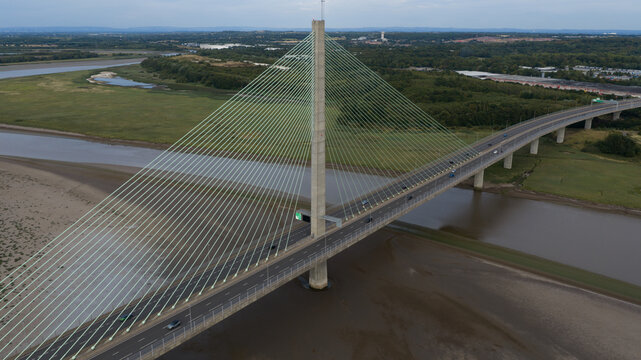 Aerial view of the Mersey Gateway Bridge, a cable-stayed bridge spanning the River Mersey with traffic flowing across, surrounded by mudflats and green landscape in Runcorn, United Kingdom.