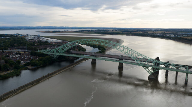Aerial view of the Silver Jubilee Bridge spanning the River Mersey with urban surroundings and calm waters in Runcorn, United Kingdom.