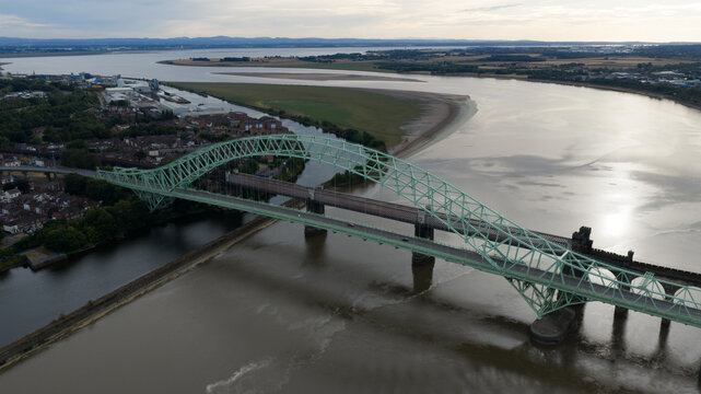 Aerial view of the Silver Jubilee Bridge spanning the River Mersey with urban surroundings and calm waters in Runcorn, United Kingdom.